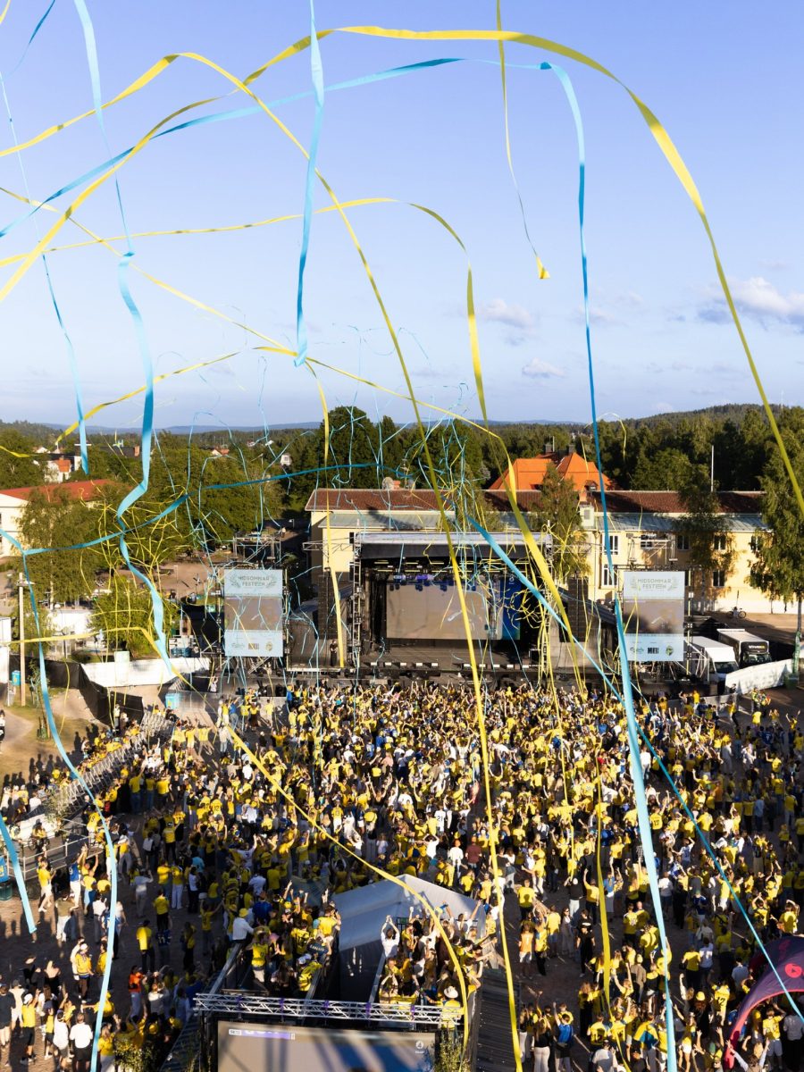 Publik i gula tröjor och blågula serpentiner framför scenen på Midsommarfesten i Leksand.